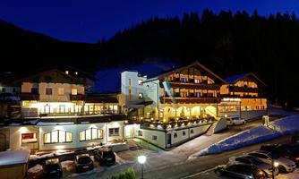 A picturesque hotel in the mountains, illuminated in the evening twilight. Snow and trees surround the building, which exudes an inviting atmosphere.