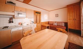 A bright kitchen with modern design and wooden cabinets. A dining table and a cozy seating area create an inviting atmosphere.