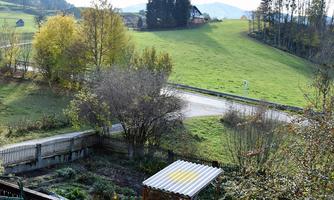 A picturesque landscape with green meadows and gentle hills. In the foreground, there are trees and a garden with a covered seating area.