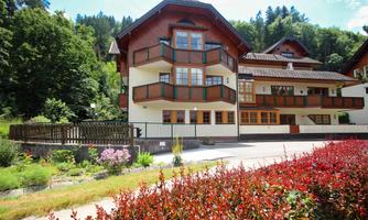 A charming building in Alpine style with several balconies. Surrounded by green trees and colorful flower beds.
