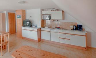 A modern kitchen with light wooden surfaces and white cabinets. It includes essential kitchen appliances and a dining area with a large table.