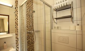 A modern bathroom with a shower cabin and bright tiles. Towels and toiletries are neatly arranged on a shelf.
