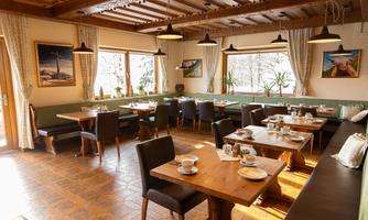 An inviting restaurant with wooden tables and cozy seating. The windows let in plenty of natural light, and the walls are adorned with beautiful pictures.