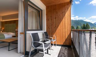 A modern balcony with two chairs and a view of the mountains. The room has large windows and a bright wood paneling.