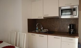 A modern kitchen unit with white cabinets, microwave, and coffee machine. There is a small dining table with white chairs.