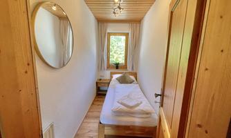 A small, bright room with a single bed and a large mirror. Natural light comes in through the window, creating a pleasant atmosphere.