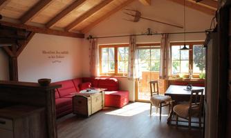 A cozy living space with wooden beams and a red sofa. Large windows let in plenty of daylight and offer a view of nature.