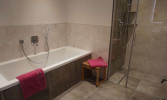 A modern bathroom with a bathtub and a separate shower. Pink towels are lying on a small wooden chair.
