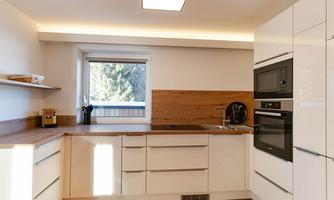 A modern kitchen with white furniture and wood accents. There is a window that lets in plenty of natural light.