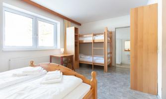 A bright and spacious bedroom with a double bed and a bunk bed. The walls are neutral, and the room has large windows that let in plenty of daylight.