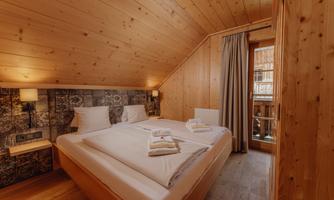 A cozy bedroom with wood paneling and a double bed. Large windows and curtains provide plenty of light and a welcoming atmosphere.