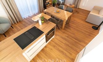 A modern kitchen with bright wooden furniture and a dining area. The room design is friendly and inviting, with plenty of natural light.