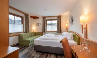 A cozy hotel room with a double bed and a seating area. A window with a view and warm lighting create an inviting atmosphere.