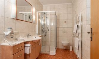 A modern bathroom with a shower, a washbasin, and a wall mirror. The walls are tiled and there is a towel radiator.