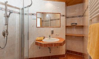 A modern bathroom with a shower and a sink. The walls are tiled in light colors and there is a large mirror.