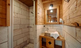 A rustic bathroom with wooden walls and tiles. There is a shower, a stone sink, and a mirror.