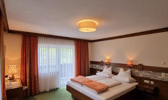A cozy hotel room with a double bed and two single beds.  
Large windows provide plenty of daylight and the green carpets give the room an inviting atmosphere.