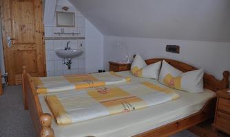 A cozy bedroom with a wooden double bed and yellow bedding. In the background, there is a sink and a wooden wardrobe.
