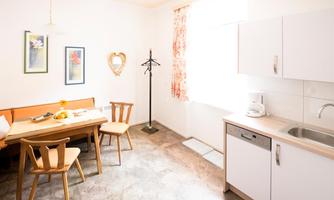A bright, welcoming kitchen with a dining table and chairs. Pictures hang on the wall and a coat rack stands beside it.
