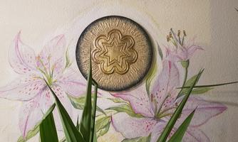 A wall with an artistic depiction of lilies and a golden, round ornament in the center. Some green plants complement the picture.