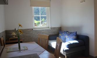 A bright, cozy living room with a blue sofa and a dining table. Beautiful sunlight floods the room through the window.