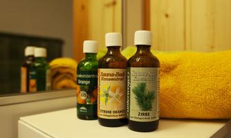 Three bottles of essential oils are standing on a white shelf, next to a yellow towel. The oils are bottled in brown glass bottles with white caps.