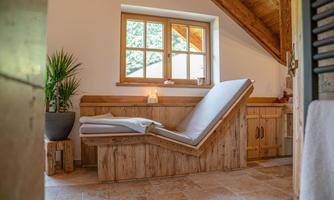 A cozy room with a wooden lounge and a large window front.  
Plants and a warm atmosphere invite you to relax.