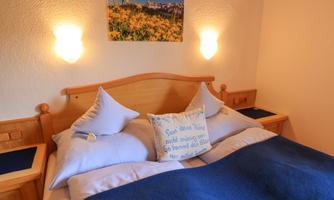 A cozy bedroom with a double bed and two pillows. On the wall hangs a picture of a beautiful landscape.