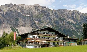 A traditional Alpine house with a beautiful porch. In the background, majestic mountains rise under a clear sky.