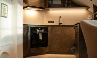 A modern kitchen under a sloped roof with dark furniture. There is a cooking area, an oven, and pleasant lighting.