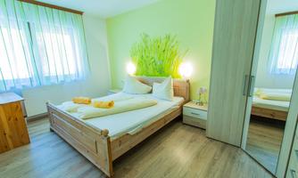 A bright bedroom with a double bed and fresh green accents. Large windows provide plenty of daylight.