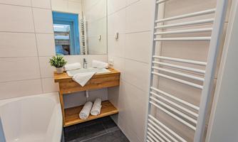 A modern bathroom with a wooden table and a mirror. Towels are neatly stacked and a green plant provides fresh accents.
