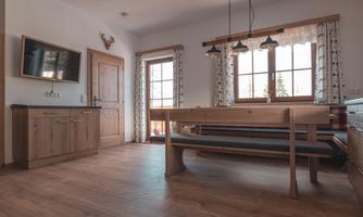 A modern living room with wooden furniture and a large table. Bright windows ensure plenty of daylight.