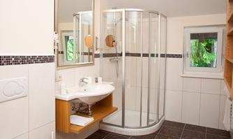 A modern bathroom with a glass shower and a sink. The walls are tiled in light colors and there is a large window with a view of the outdoors.