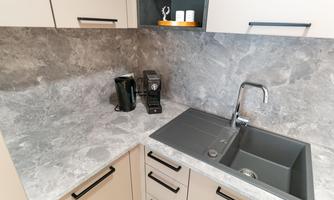 A modern kitchen with a gray countertop and a dark sink. On the countertop, there is a kettle and a coffee maker.