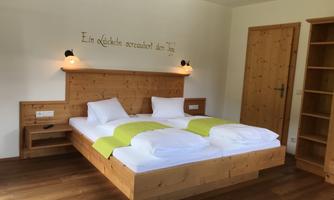 A cozy room with a wooden double bed and fresh, bright bedding. There is a beautiful saying on the wall and the room has warm lighting.