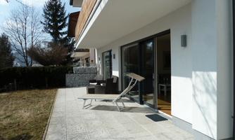 A modern terrace with loungers and large window fronts. The room is bright and offers a view of the garden.
