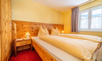 A cozy bedroom with two single beds and wooden paneling. The walls are painted yellow, and there are windows with curtains.