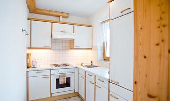 A modern kitchen with white furniture and wooden details. It includes a stove, a sink, and plenty of storage space.