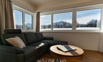 A bright and modern living room with a cozy sofa and a round table. Through the windows, one looks out at snow-covered mountains and forests.
