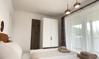 A modern bedroom with two beds and neutral colors. Large windows let in plenty of light and offer a view outside.