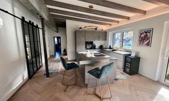 A modern kitchen with wooden ceiling beams and a stylish kitchen island. The decor is bright and inviting, with a large window that lets in natural light.