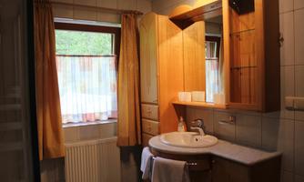 A bathroom with a sink, a mirror, and a wooden cabinet. Bright curtains hang in front of the window.