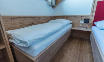 A simple bedroom with a single bed and wood paneling. The atmosphere is calm and cozy.