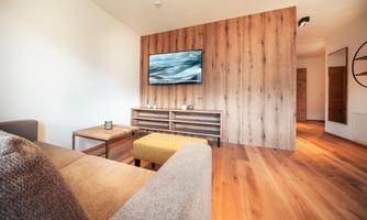 A modern living room with a cozy sofa and a wooden table. A television hangs on the wall and the floor is made of wood.