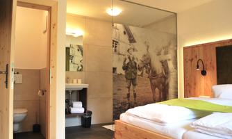 A modern hotel room with wooden details and a double bed. In the background, a wall is decorated with a historical photo.