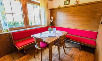 A cozy dining area with a round table and a red bench. Bright windows let in plenty of daylight.
