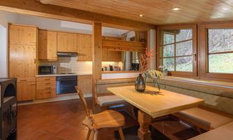 A cozy kitchen with wooden shelves and a large dining table.  
Large windows offer a view of the nature outside.