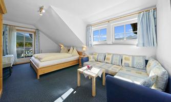 A cozy room with a double bed and a seating area. Large windows offer a view of the surroundings.