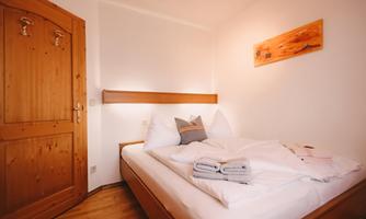 A cozy bedroom with a double bed and wooden furniture. The walls are painted light and there is an artistic wooden picture in the room.